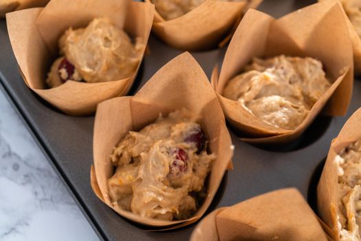 Scooping dough into muffin cups to bake cranberry muffins.