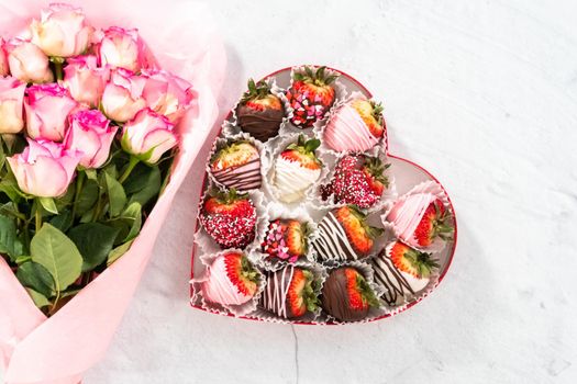 Flat lay. Bouquet of fresh pink roses and chocolate dipped strawberries on a white background.