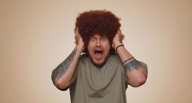 Stressed depressed adult man 30 years old in green t-shirt expresses his fear and waves his hands away from danger, waving no. Scared fearful young guy isolated alone on beige studio wall background
