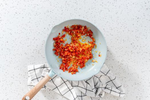 Flat lay. Frying onion and red bell pepper in olive oil on a nonstick frying pan to bake turkey empanadas.