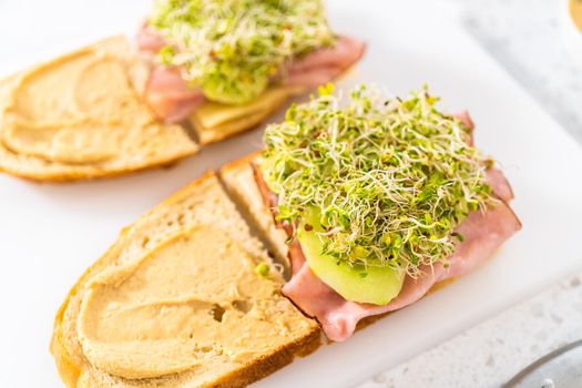 Assembling ham, cucumber, and sprout sandwiches on the white cutting board.