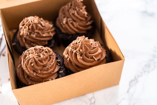 Packaging chocolate cupcakes with chocolate ganache frosting into a paper cupcake box.