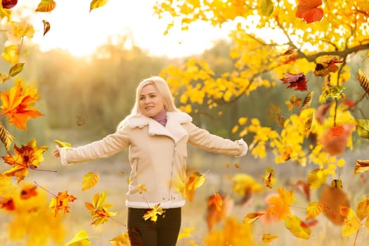 Beautiful girl walking outdoors in autumn. Smiling girl collects yellow leaves in autumn. Young woman enjoying autumn weather. High quality photo