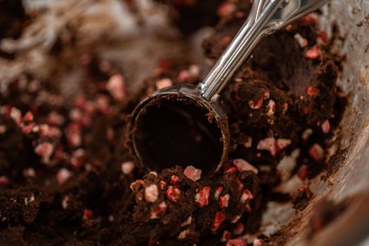 Scooping chocolate cookie dough with dough scoop to bake chocolate cookies with peppermint chips.