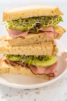 Stack of ham, cucumber, and sprout sandwiches on the white plate