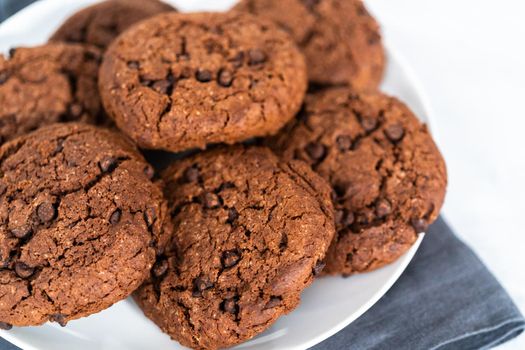 Freshly baked double chocolate chip cookies on a white plate.