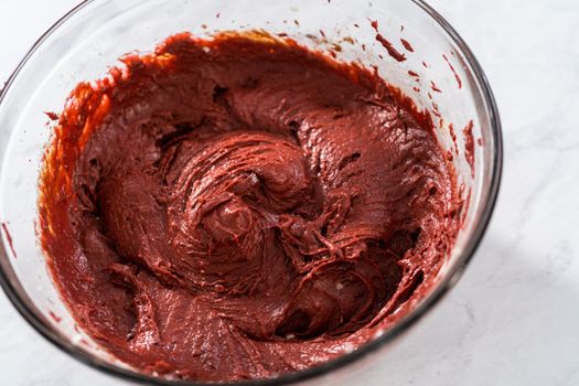 Mixing ingredients in a large glass mixing bowl to bake red velvet bundt cake with cream cheese glaze.