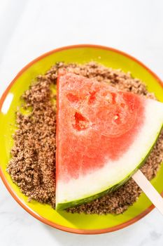 Dipping watermelon pops into the chili lime salt to prepare Mexican watermelon pops.