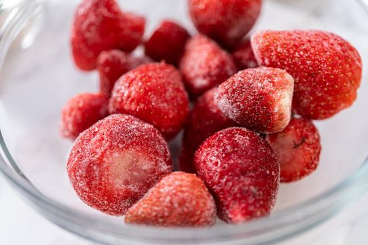 Measured ingredients in a glass mixing bowl to prepare a strawberry banana smoothie.