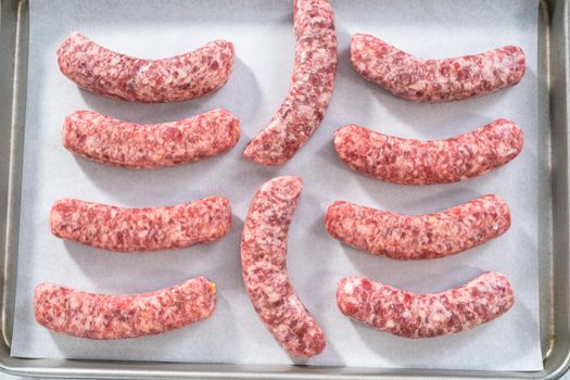 Raw beer bratwursts on a baking sheet lined with parchment paper ready to be cooked in the oven.