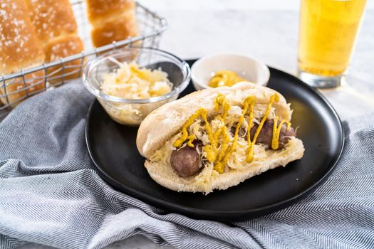 Beer brats with sauerkraut on large bun drizzled with mustard.