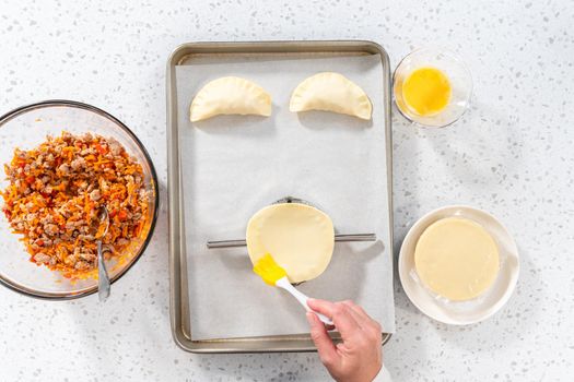 Flat lay. Brushing uncooked turkey empanadas with egg wash.