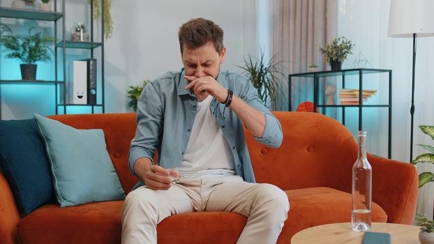 Sad worried young man looks pensive of unrequited love, suffers from unfair situation, drinking vodka. Problem, break up, depressed feeling bad annoyed, burnout, bankruptcy. Guy sitting at home room
