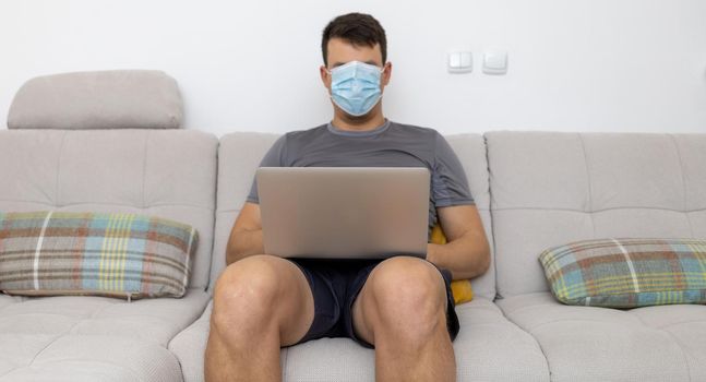 mask covering whole face man with laptop on sofa. High quality photo