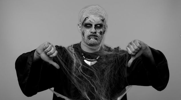 Scary man in carnival costume of Halloween crazy zombie undead with bloody wounded scars face showing thumbs down sign gesture, expressing discontent, disapproval, dissatisfied, dislike. Chroma key