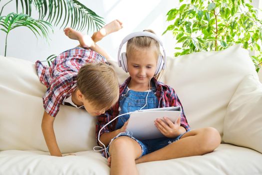 Cute brother and sister with headphones enjoying tablet at home. family, children, technology and home concept