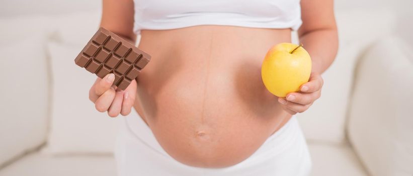 A pregnant woman is holding an apple and a bar of chocolate. The ninth month of pregnancy