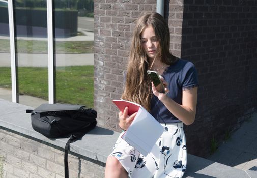 teenage girl student copying text using phone to send to her classmate using mobile phone technology. High quality photo