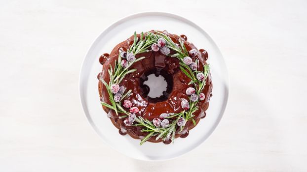 Step by step. Flat lay. Chocolate bundt cake with chocolate frosting decorated with fresh cranberries and rosemary covered in a white sugar.