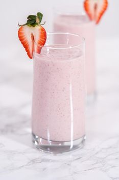 Freshly made healthy breakfast strawberry banana smoothie garnished with fresh strawberry and paper straw.