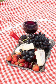 summer picnic on a green lawn with red wine, cheese and fresh berries, grapes, cherries, strawberries, summer vacation. High quality photo