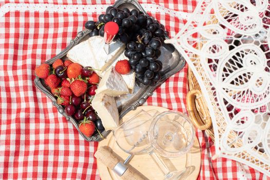 summer picnic on a green lawn with red wine, cheese and fresh berries, grapes, cherries, strawberries, summer vacation. High quality photo