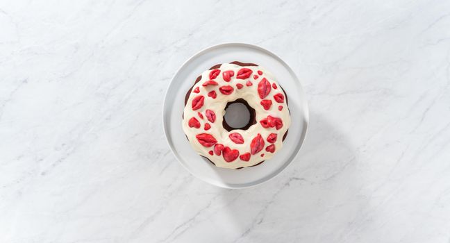 Flat lay. Decorating red velvet bundt cake with chocolate lips and hearts over cream cheese glaze.