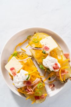 Pressure Cooker Baked Potatoes. Garnished large baked potatoes with butter, sour cream, cheese, and bacon bits on a white plate.