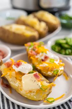 Pressure Cooker Baked Potatoes. Garnished large baked potatoes with butter, sour cream, cheese, and bacon bits on a white plate.