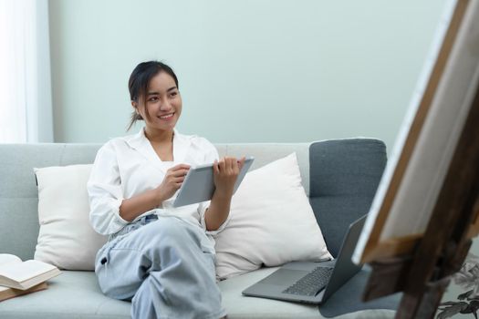 Portrait of an Asian woman using a tablet to paint artwork on a sofa