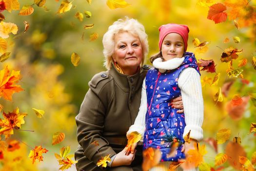Granddaughter and grandmother hugging while sitting on a bench in the autumn forest . High quality photo