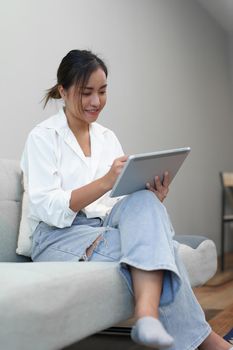 Portrait of a young Asian woman sitting on the sofa using a tablet