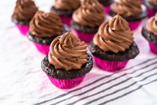 Piping chocolate ganache frosting on top of chocolate cupcakes.