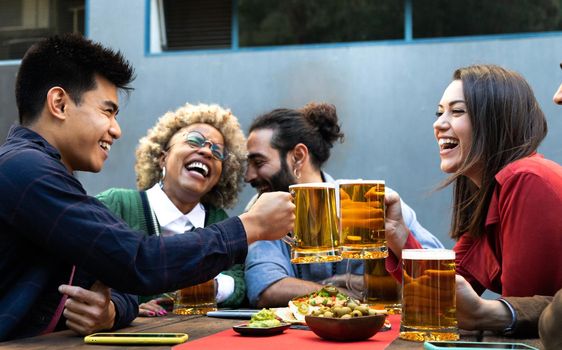 Cheers. Multiracial group of happy and smiling friends toast with beer and laugh together in a bar outdoors. Friendship and happiness concept.