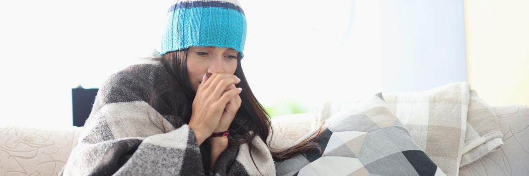 Sick woman in hat sitting under blanket at home. Seasonal viral diseases concept