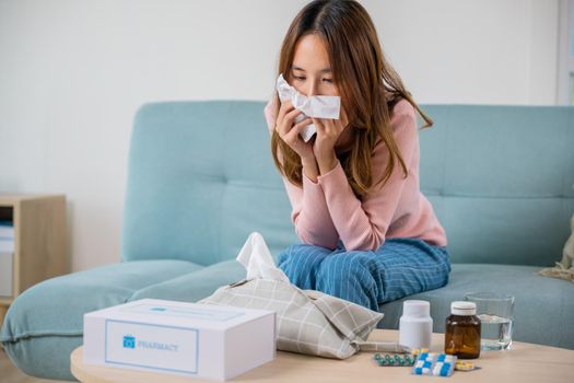 Sick woman. Asian young girl cold sick she sneeze with tissue paper on sofa, beautiful female health problem blowing nose use pharmacy kit box delivery service from hospital, delivery pharmacy concept