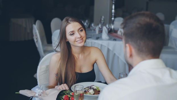 Attractive girlfriend and boyfriend in fance clothing are clinking glasses, drinking champagne and talking on romantic date in classy restaurant. Romance, love and fine dining concept.