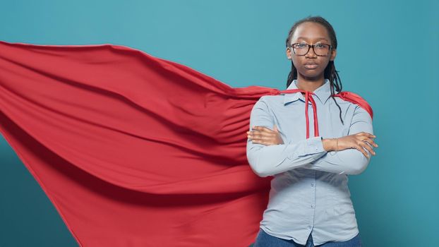 Portrait of female superhero wearing red cape costume from cartoon or comic book, showing strength and motivation. Woman posing as hero character with cloak, feeling confident.