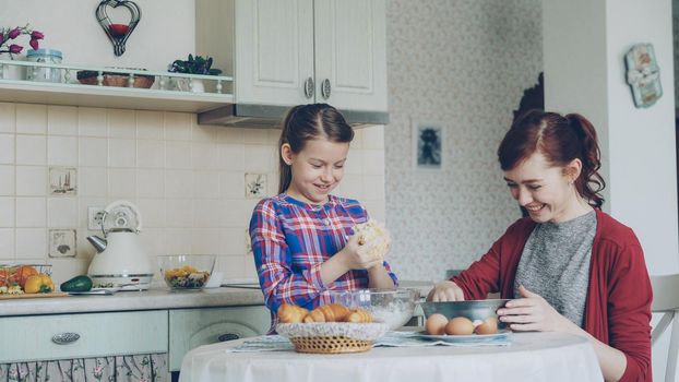 Little cute girl helping her mother in the kitchen stirring dough for cookies into bowl. Mom have fun smearing daughter nose with flour and they laughing . Family, food, home and people concept