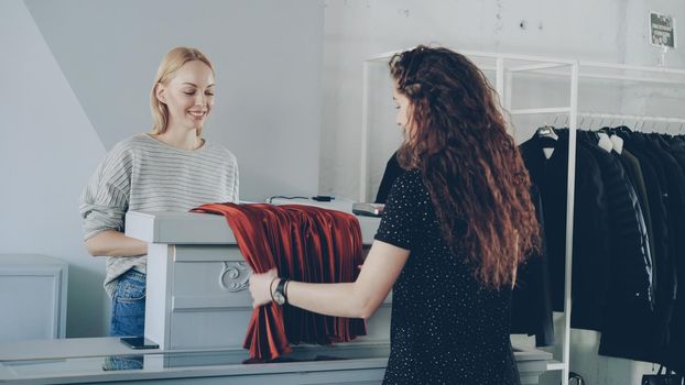 Saleswoman is folding clothes and putting it in bag, then giving it to shopper