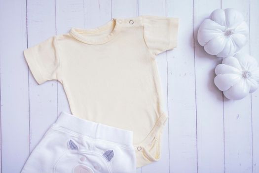 Yellow baby bodysuit mockup for logo, text or design on wooden background with pumpkins top view.