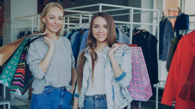 Portrait of beautiful young women are standing with lots of paper bags in their hands in luxurious women's clothes boutique. Fashionable clothes, bags, shoes and baloons in background.