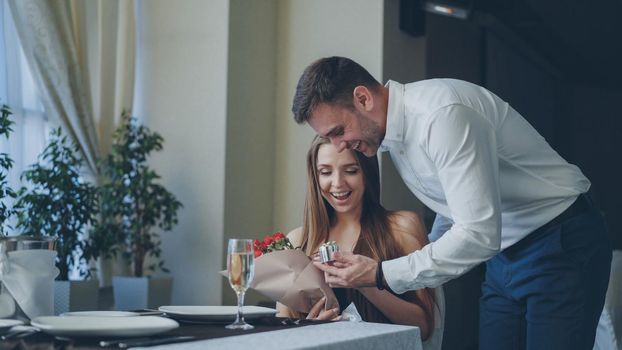 Happy girlfriend is getting flowers and present from her loving boyfriend after waiting for him alone in restaurant. Romantic relationship, gifts and fine dining concept.