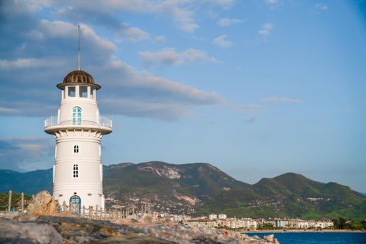 White port lighthouse on the background of mountains and sky and sea. Copy space
