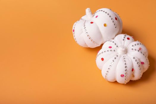 White decorative textile pumpkins with shiny stones on orange background with copy space. Autumn harvest and thanksgiving day concept.