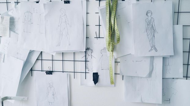 Black and white sketches, drawings and notes with measurements of women's garments on wall in clothing design studio. Creating new collection of stylish clothes concept.