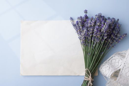 Lavender flowers in a bouquet with blank sheet old paper for text and light from window on colored background. High quality photo