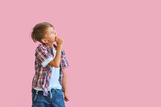 Young happy boy dressed in jeans, a white T-shirt and a plaid shirt isolated on pink background with copy space