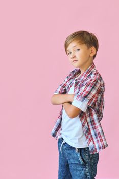 Young happy boy dressed in jeans, a white T-shirt and a plaid shirt isolated on pink background with copy space
