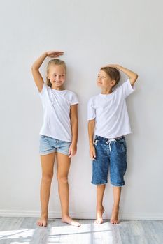 Cool kids, little boy and girl measure their height and compare, have fun near white wall